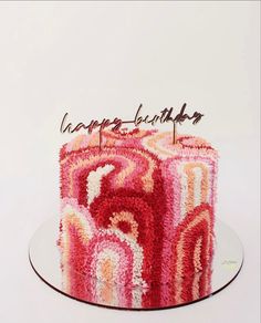 a birthday cake decorated with pink and red swirls on a glass plate, topped with a happy birthday candle