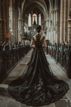 a woman in a black dress standing at the end of a church aisle with her back to the camera