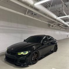 a black car is parked in an empty parking garage with white walls and exposed pipes