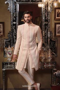 a man standing in front of a mirror wearing a pink sherve coat and white pants