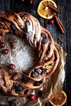 an orange and cranberry cinnamon roll wreath on top of wax paper next to sliced oranges