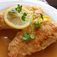 a white plate topped with chicken covered in gravy and garnished with lemon wedges