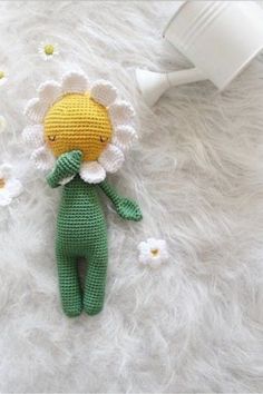 a crocheted doll laying on top of a fluffy white blanket next to a coffee cup