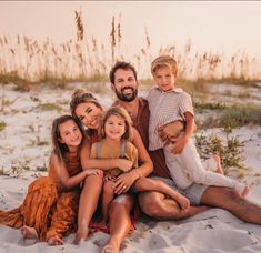 a group of people sitting on top of a sandy beach next to tall grass and sea oats