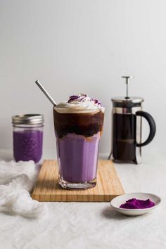 a glass with purple liquid and whipped cream in it sitting on a wooden cutting board