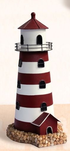 a small red and white lighthouse sitting on top of a pile of rocks next to a wall