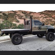 the truck is parked on the side of the road in front of some hills and trees