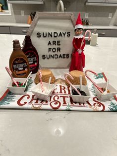 an elf is standing next to some food on a counter top with a sign that says sunday's are for sundaes