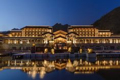 a large building sitting on top of a lake next to a tall mountain covered in lights