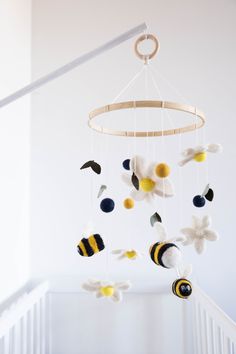 a baby crib mobile with bees and flowers hanging from it's side in a white room