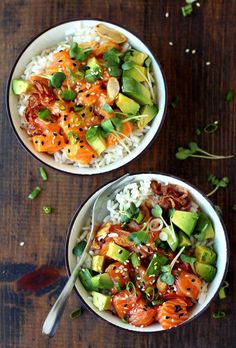 two bowls filled with rice and vegetables on top of a wooden table