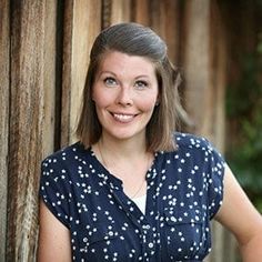 a woman standing in front of a wooden wall with her arms crossed and smiling at the camera