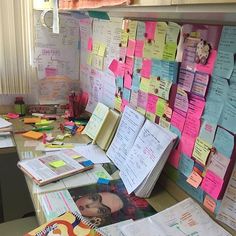 a cluttered desk with lots of papers and notes attached to the wall behind it