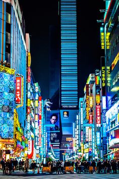 a city street filled with lots of tall buildings and people walking around it at night