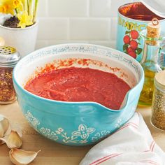 a blue bowl filled with red sauce next to garlic and seasonings on a counter