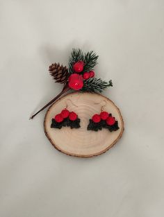 a piece of wood with red berries and pine cones on it, sitting on top of a white surface