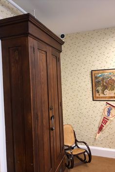 an armoire in the corner of a room next to a chair and wallpaper