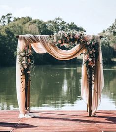 an outdoor wedding ceremony setup with flowers and draping on the water's edge