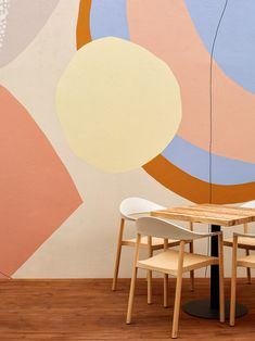 a table and chairs are in front of a wall with an abstract painting on it