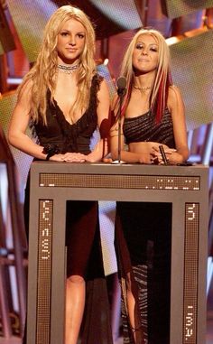 two women standing at a podium in front of a microphone and another woman with long blonde hair