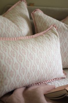 three pillows and a book on a bed with pink linens in the foreground