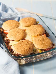 four hamburger sliders in a glass casserole dish on a blue tablecloth