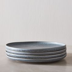 four gray plates stacked on top of each other in front of a white wall and floor