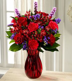 a vase filled with red and purple flowers on top of a wooden table next to a window