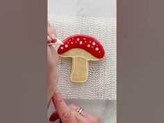 a hand holding a cookie with a red mushroom on it and white polka dots around the edges