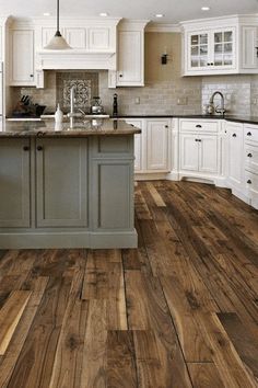 a large kitchen with white cabinets and wood flooring on the walls, along with an island in the middle