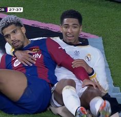 two soccer players are sitting on the ground together and one is holding his arm around the other's neck