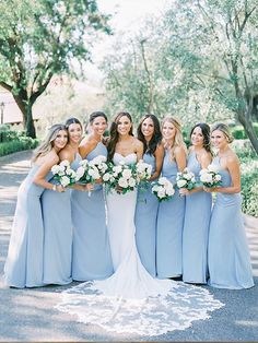 a group of women standing next to each other in front of trees and bushes with bouquets