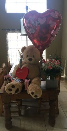 a large teddy bear sitting on top of a wooden table holding a heart shaped balloon