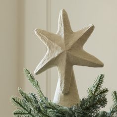 a white star ornament hanging from a christmas tree with pine needles on it