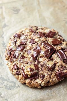 an oatmeal cookie with chocolate chips and nuts sitting on a piece of parchment paper