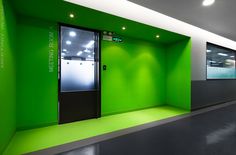 an empty room with green walls and black doors on the wall is lit by recessed lights