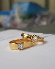 two gold rings with diamonds on top of a piece of paper next to a pen