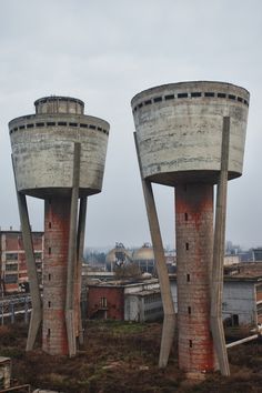 two water towers in the middle of a field with buildings in the backgroud