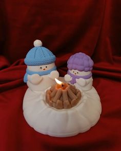 two small snowmen sitting next to a lit candle