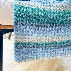 a blue and white crocheted blanket sitting on top of a wooden floor next to a chair