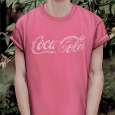 a man wearing a pink coca - cola t - shirt standing in front of flowers