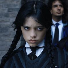 two people standing next to each other in front of a brick wall wearing school uniforms