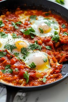 two eggs are in a skillet with tomato sauce and parsley on the side