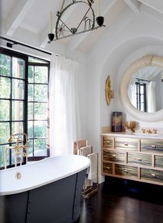 a bath tub sitting next to a window with a mirror on the wall above it