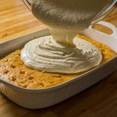 a person pouring cream on top of a cake in a pan