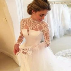 a woman in a white wedding dress looking down at her hand and wearing a long sleeved lace top