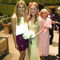 two women standing next to each other in front of a room full of people wearing dresses