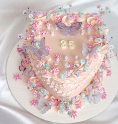 a heart shaped cake with butterflies and flowers around it on a white tableclothed surface