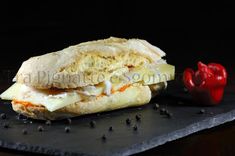 a sandwich with meat, cheese and tomato on a slate board next to peppercorst