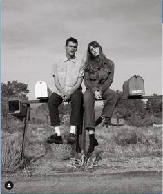 black and white photograph of two people sitting on mailbox's in the middle of nowhere